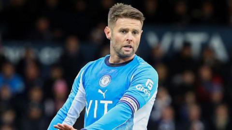 Ollie Norwood, in blue Stockport shirt with captain's armband
