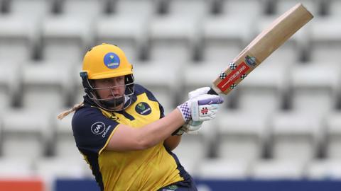 Abbey Freeborn plays a hook shot for Glamorgan in yellow kit