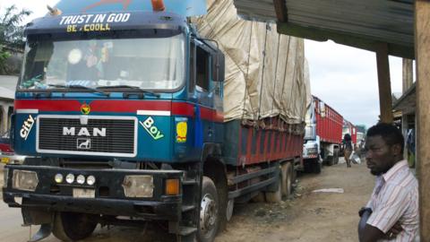 A file photo of a truck driver standing next to a lorry which is stuck at the border between Ivory Coast and Ghana because the border was closed. From October 6, 2012.