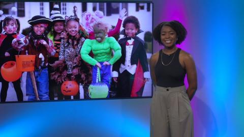 Emma-Louise in the studio, kids in halloween costumes in the screen