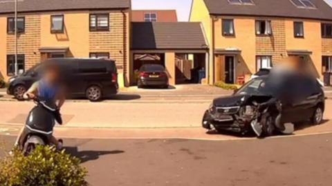 A damaged car and a moped in a street in Northstowe