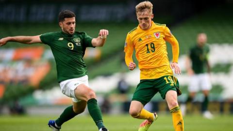 Matt Smith in a yellow Wales shirt controls the ball under pressure from the Republic of Ireland's Shane Long