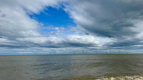 Mainly cloudy sky over the sea with wind turbines in the distance