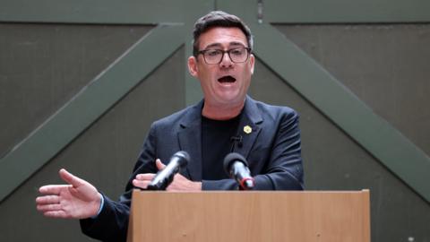 Burnham speaking at lectern, moving his hands to the side