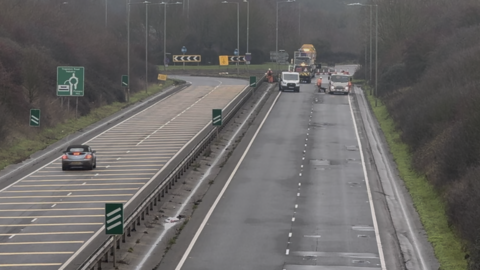 Work being carried out to repair potholes on a dual carriageway. One side of the road is closed as workmen carry out the repairs.