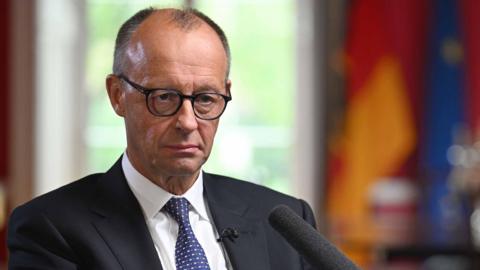 Germany's chancellor sits in a dark jacket and tie 