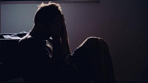 silhouette stock image of a man sat on the floor with his head in his hands, appearing in distress