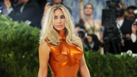 Kim Kardashian with long, blonde hair, wearing a metallic orange breastplate as she poses at the Met Gala.