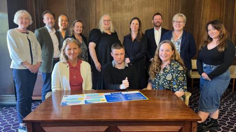 A group of people standing and seated around a table, which the new strategy is placed on.