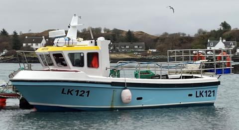 A small fishing boat sitting at sea. It is light blue in colour and has LK121 written down the side. 