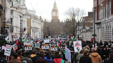 Protesters hold placards and wave Palestinian flags as they take part in a protest in central London. Big Ben is seen in the background 