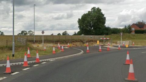 A road with traffic cones on with a view of some fences with a field behind it where the homes will go.