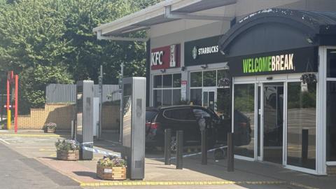 Entrance to service stations with Welcome Break sign and Starbucks and KFC visible. There is police tape across the front.