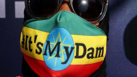 A person wearing a face mask that says 'it's my dam'