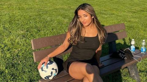 Simran Sandhu sitting on a park bench holding a football