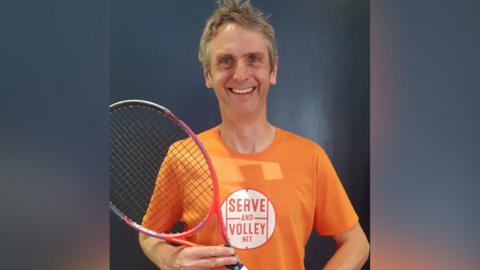 Rob Salmon, wearing an orange t-shirt and holding tennis racket
