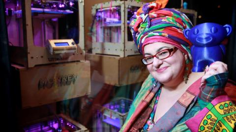 Camila Batmanghelidjh, the founder and chief executive of Kids Company, wearing colourful clothes and a colourful headdress. She is holding a 3D printed toy at the launch of Print Happiness, a pop-up store in London's Soho.