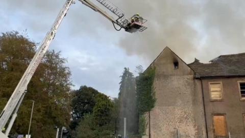 Firefighter sprays water from an aerial platform on to fire in derelict building