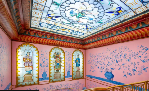 A room in the pavilion, which has three stained glass windows on the back wall and a stained glass sunroof. The room itself is bright pink with a clashing red border and a blue design of a vase with flowers in