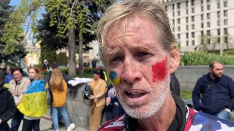 This screengrab taken from AFPTV shows Ryan Wesley Routh at a protest supporting Ukraine in April 2022.  Routh is wearing an American flag shirt and has face paint in the colours of the Ukrainian flag on his cheek.