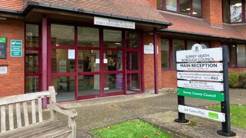 The main entrance to the offices at Surrey Heath Borough Council in Camberley. There is a bench and also a sign describing the different services the council offers.