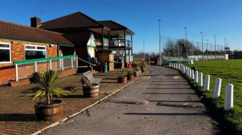A pub seen from the outside next to a green field. The sky is blue and the sun is shining.