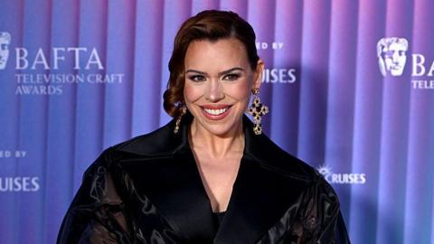 Billie Piper smiles on the red carpet wearing a black coat.