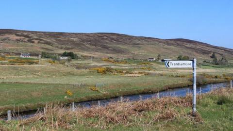 Soidhne Tranndal Mòr ann an Cataibh, le abhainn agus taighean agus cnuic air là math