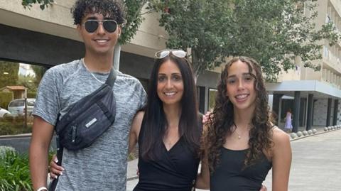 Natalie Kerr stands between her two children, smiling with her arms around them