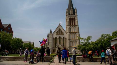 Thames Town in China. It is a replica village which features various English landmarks and buildings, including a replica Christ Church which is found in Clifton, Bristol. The replica church has a tower with lots of windows. There are many people walking around and near the Chinese building.