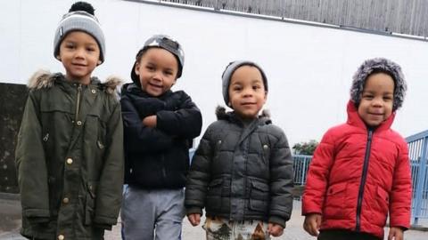 Kyson and Bryson Hoath, aged four (left), and Leyton and Logan Hoath, aged three (right). They are all stood smiling at the camera wearing puffer jackets with hats on.