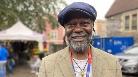 Levi Roots dressed in a checked jacket and blue hat 