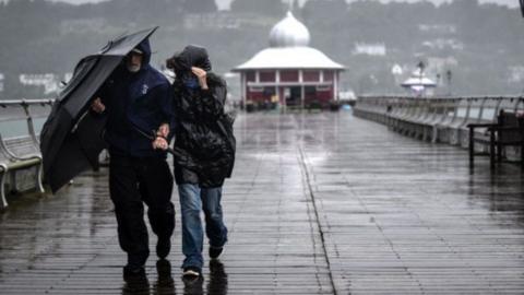 Two people sharing an umbrella on a wet and windy pier