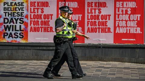 A pair of police officers walking with pink and red advert billboards behind them