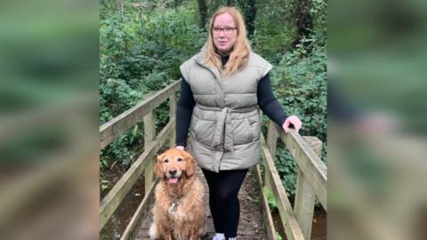 Angharad Paget-Jones standing on a wooden bridge with her guide dog Tudor