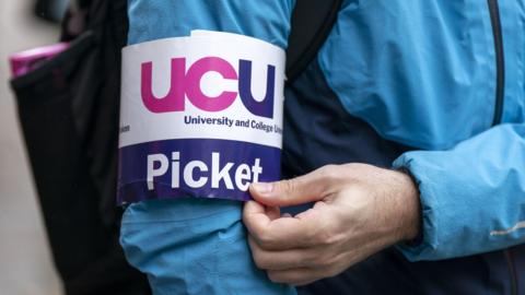 A striking lecturer wearing a UCU armband in white and navy blue with purple writing on it.