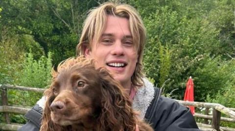 Nicholas Galitzine holding a brown spaniel type dog. 