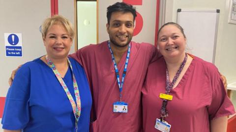 Theatres ophthalmic team leader Emma Langdon-Manning, ophthalmology consultant and retinal surgeon Ahmed Javed and registered nurse associate Leanne Mosavie. Mr Ahmed has his arms around his colleagues. They are standing next to each other wearing lanyards with ID badges