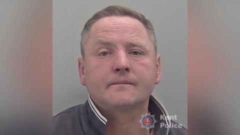 A mugshot of a man. He is wearing a collared jacket.