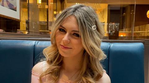 Isla Sneddon, a teenage girl with long blonde hair and wearing a pink top. She is smiling at the camera.