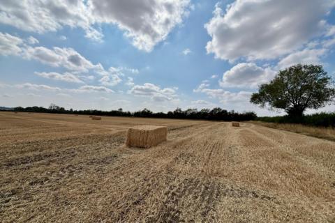Harvested field with straw bales beneath a partly cloudy sky in Fenny Compton, Warwickshire
