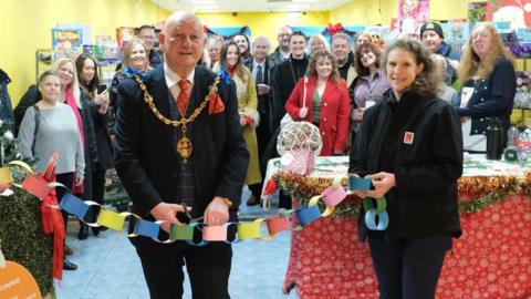 A man cutting a ribbon, with a group of people behind. 