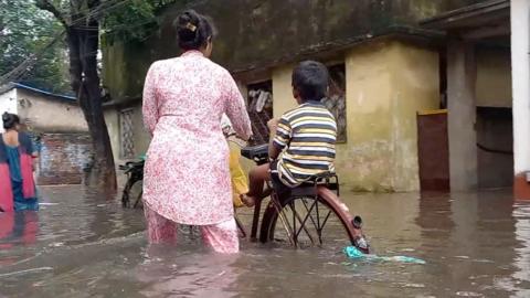 Woman and a child use cycle to pass through knee-deep waters in India's Kolkata city