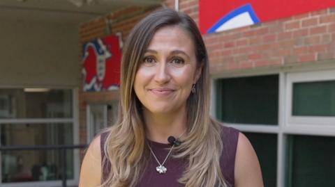 Sarah Dawkins, BBC Sport reporter smiling down the lens wearing a maroon top and silver necklace