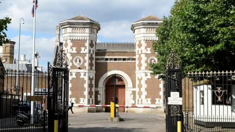 Wormwood Scrubs exterior - a red brick Victorian building with a traffic barrier outside