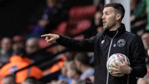 Walsall head coach Mat Salder issues instructions from the touchline with a ball under his arm