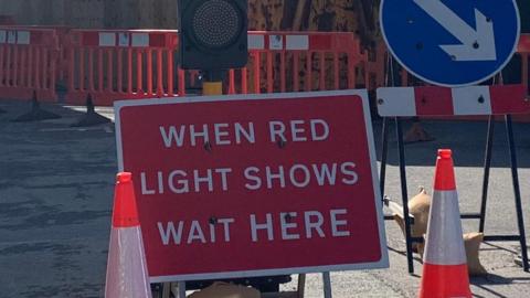 A red road sign that says when red light shows wait here that has traffic cones either side of it.
