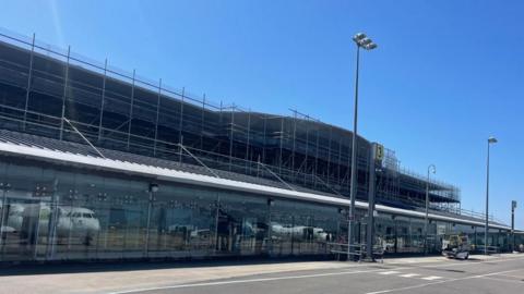 An airport surrounded in scaffolding with reflections of aeroplanes in the panes of the glass.