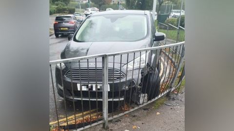 A silver Ford car that has crashed into a fence, with significant damage to the front left-hand side.