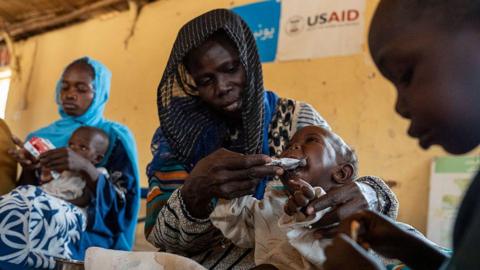 Woman feeds baby with USAID sign in background